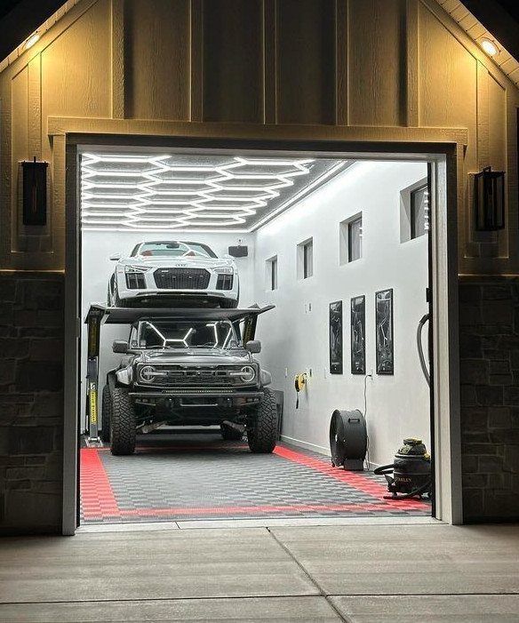 Two vehicles, one on a hydraulic lift, inside a brightly lit modern garage with geometric ceiling lights.