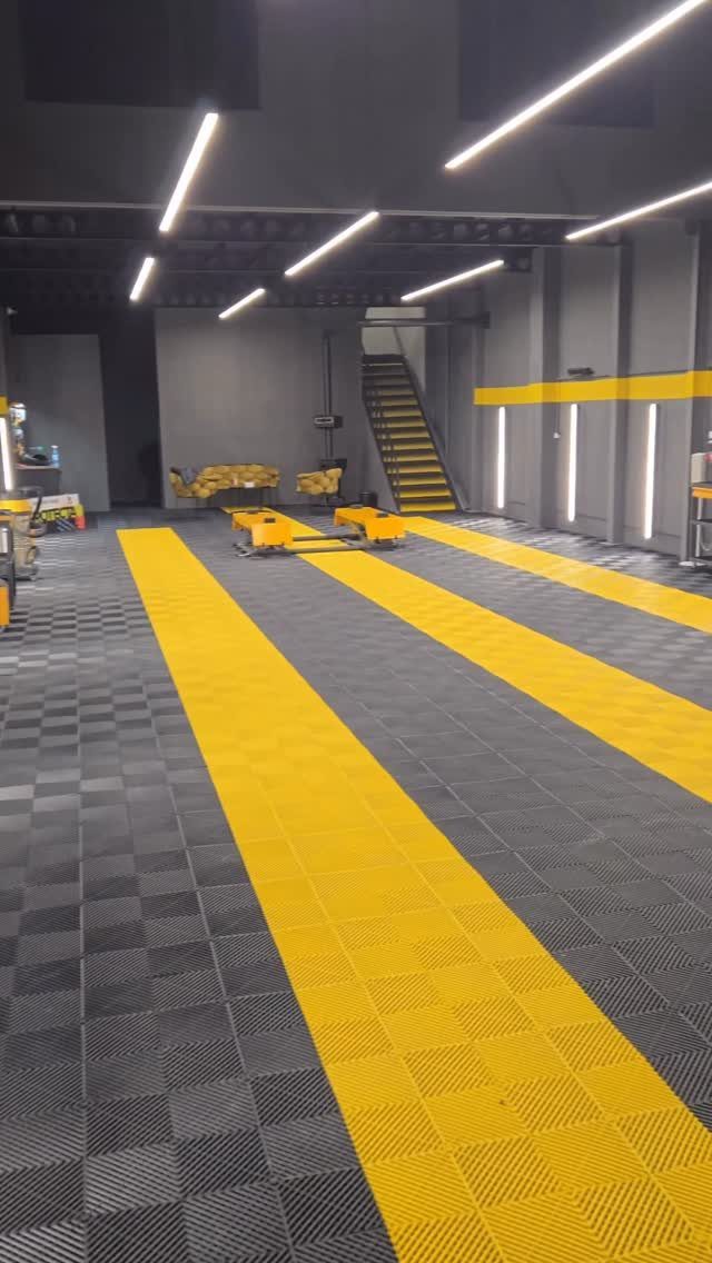 A modern garage interior featuring a grey and yellow checkered tiled floor and bright linear lighting.