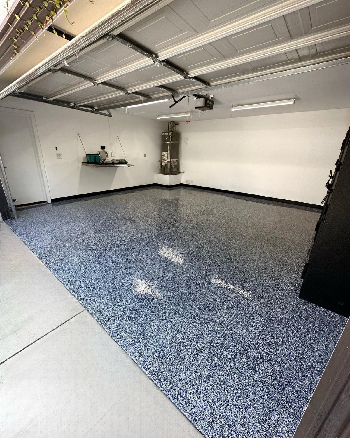 A large garage with a blue and white speckled polyaspartic coated floor and white walls.