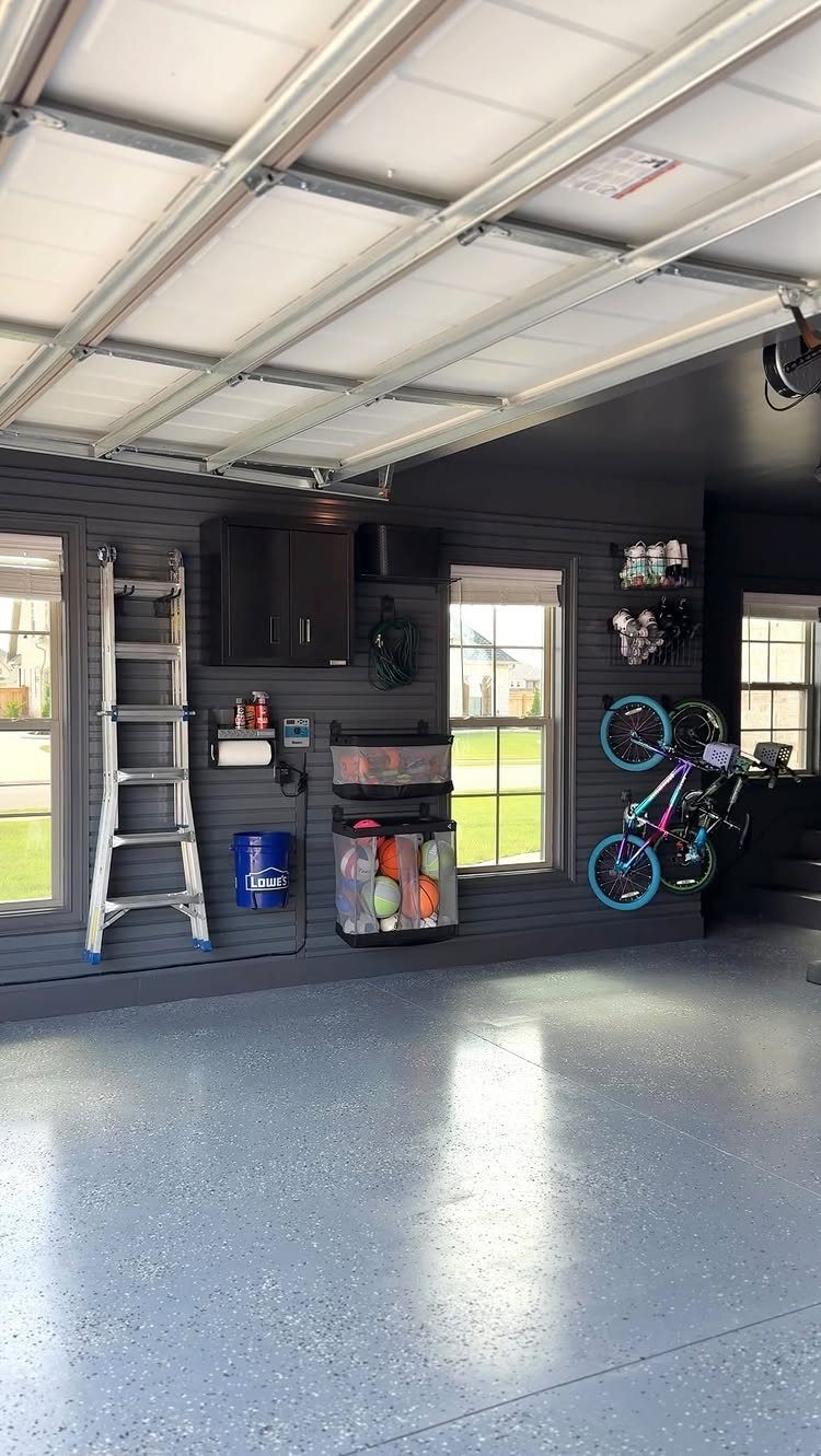 Organized garage interior featuring dark grey walls, epoxy flooring, storage cabinets, and bicycles hanging on the wall.