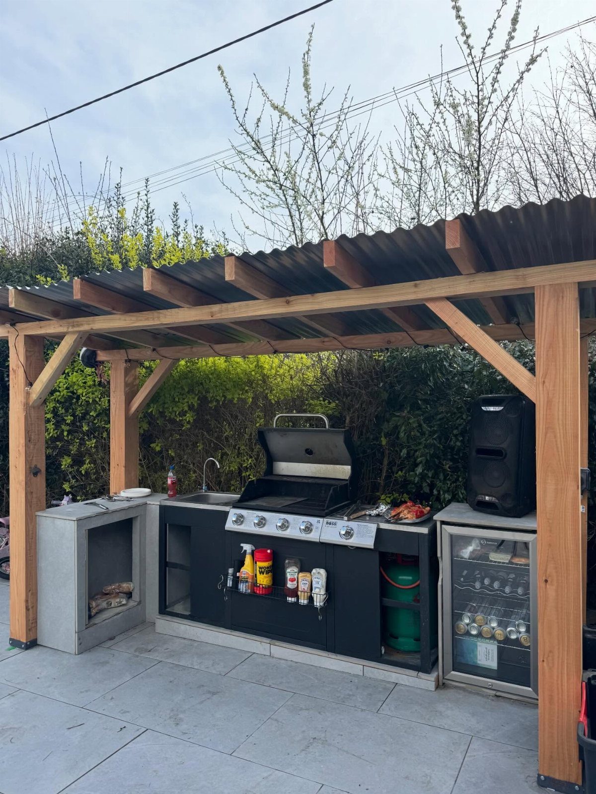 A wooden pergola sheltering a modern outdoor kitchen with a built-in grill and cabinetry.