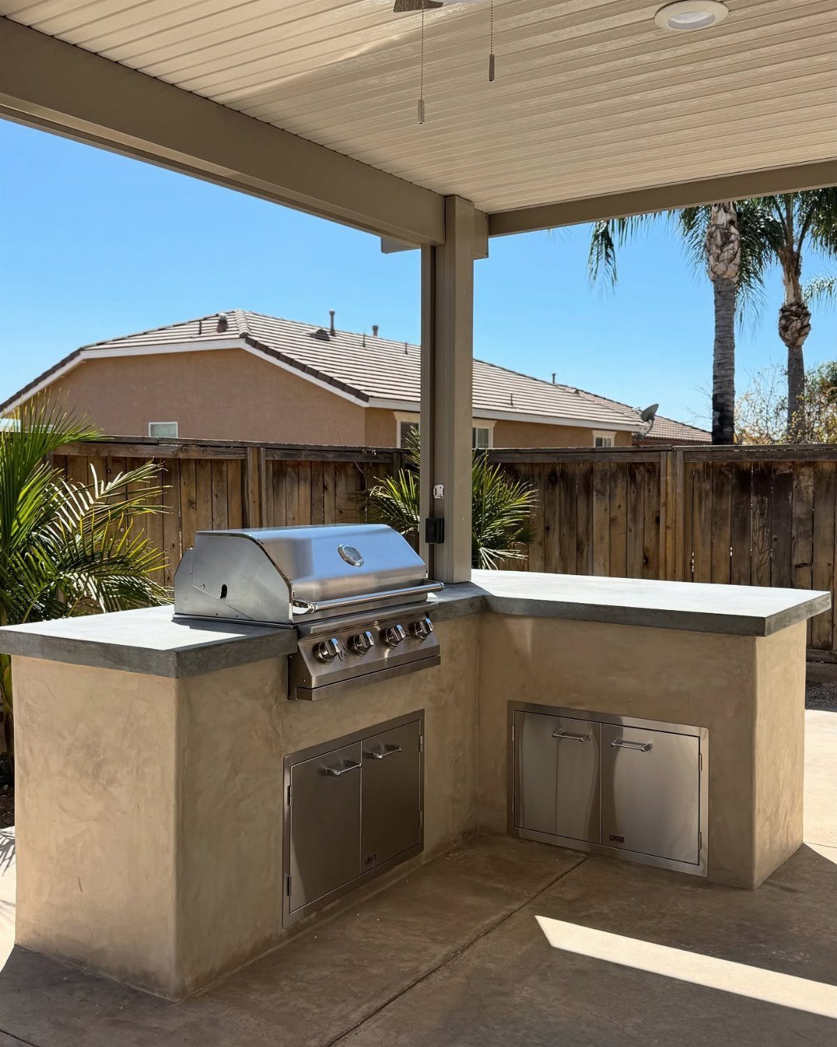 Stainless steel gas grill built into a stucco outdoor kitchen island with grey countertops.
