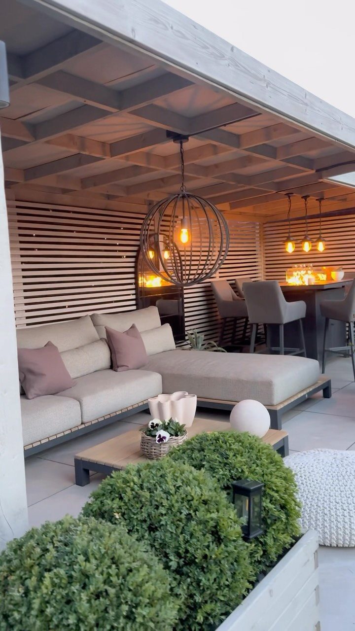 Beige L-shaped outdoor sectional sofa with pillows sits on a patio near green shrubs.
