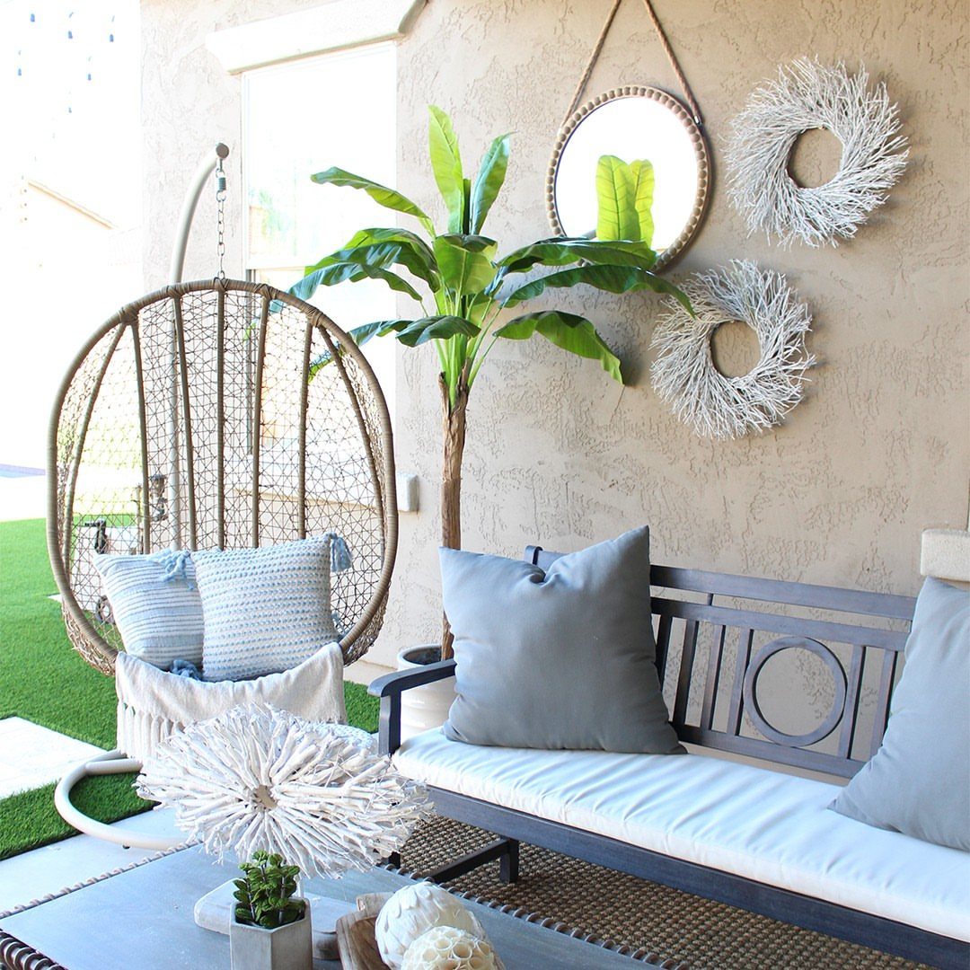 A hanging egg chair and grey bench with blue pillows on a patio.