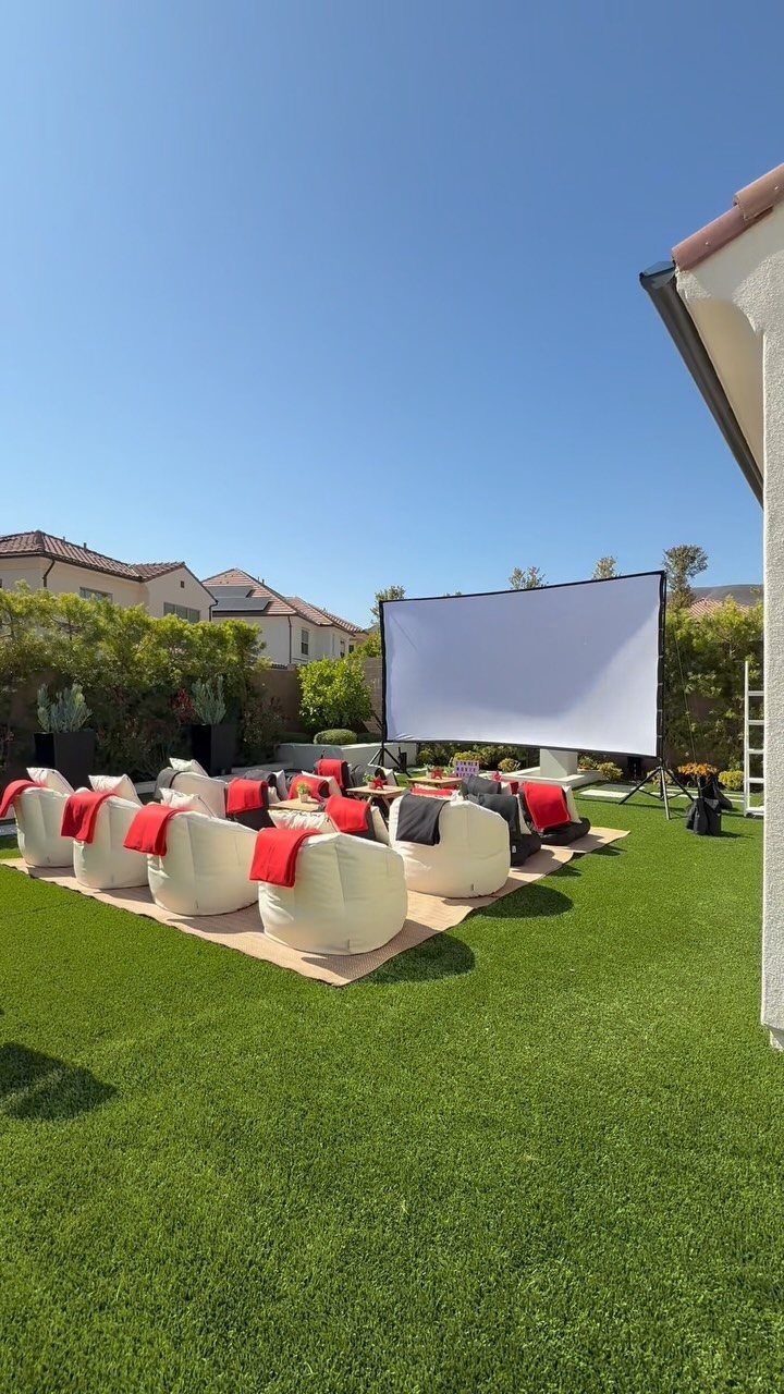 White bean bag chairs with red blankets arranged on a lawn facing a large projector screen.