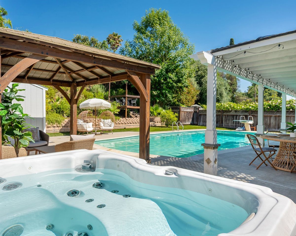 White hot tub in the foreground overlooking a turquoise swimming pool and patio area.