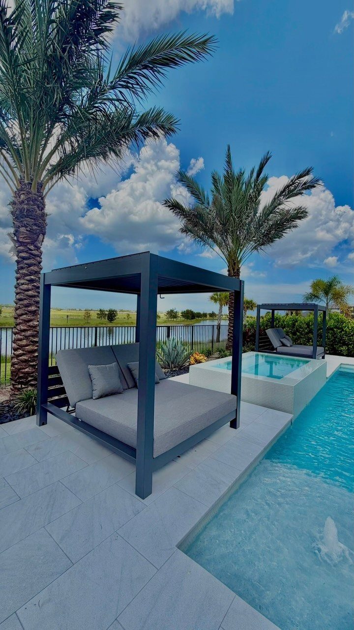Modern black cabanas with grey daybeds situated on a white patio next to a swimming pool.