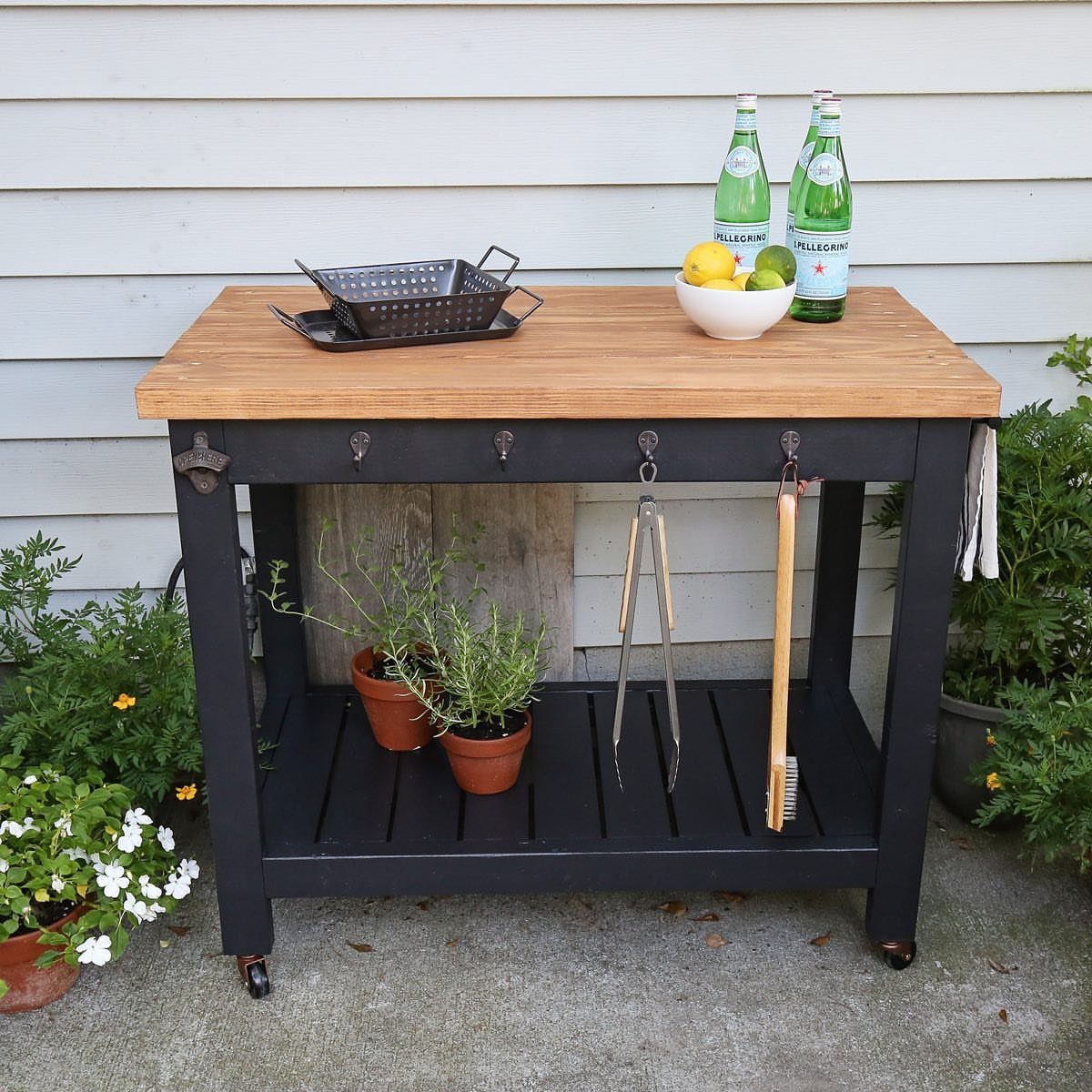 A black wooden cart with a teak top holding sparkling water and citrus fruit.