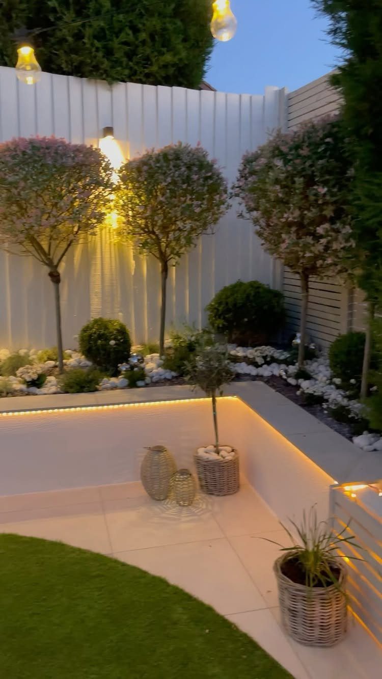 Small trees and white flowers planted along a white fence in a landscaped backyard.