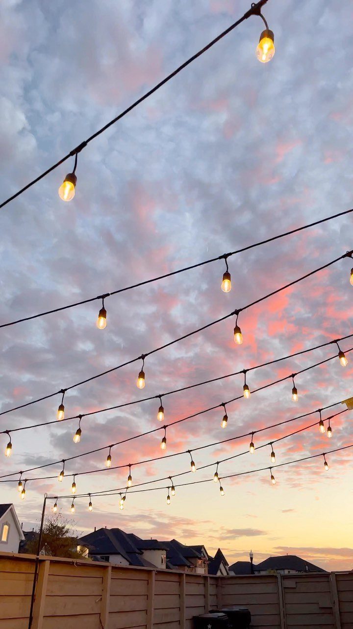 String lights with glowing bulbs hang against a sunset sky with pink clouds.