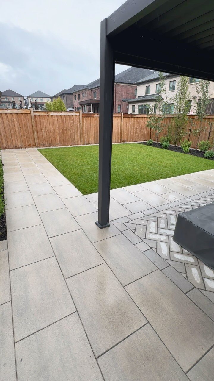 Light grey stone pavers form a patio surrounding a manicured green lawn and wooden fence.