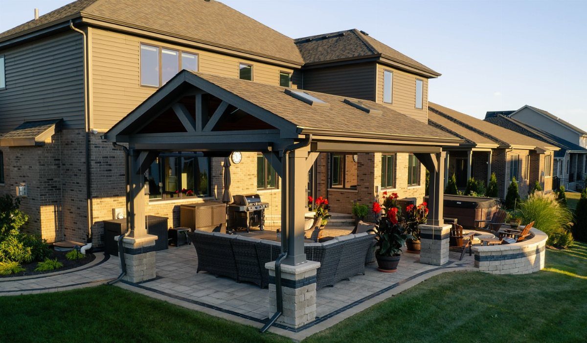 A large grey wooden pergola provides shade over a stone patio with outdoor furniture.