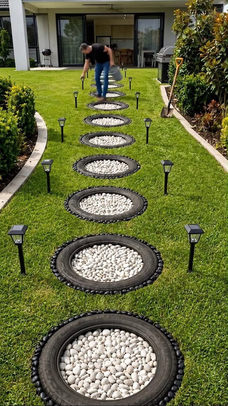 Black tires filled with white stones form a decorative path across a green backyard lawn.