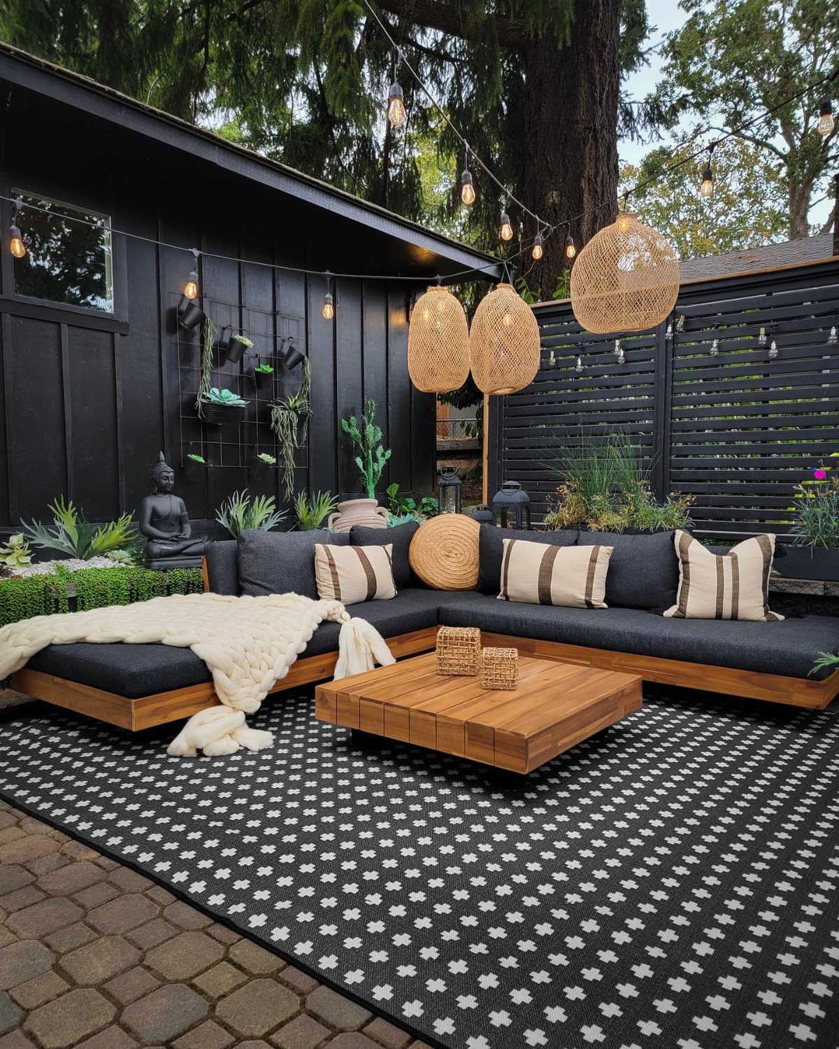 A black and white patterned outdoor rug under a modern wooden sectional sofa and coffee table.