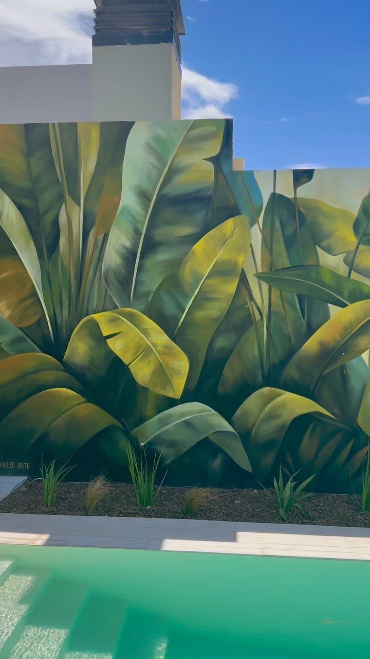 Tropical leaf mural painted on a wall behind a turquoise swimming pool.