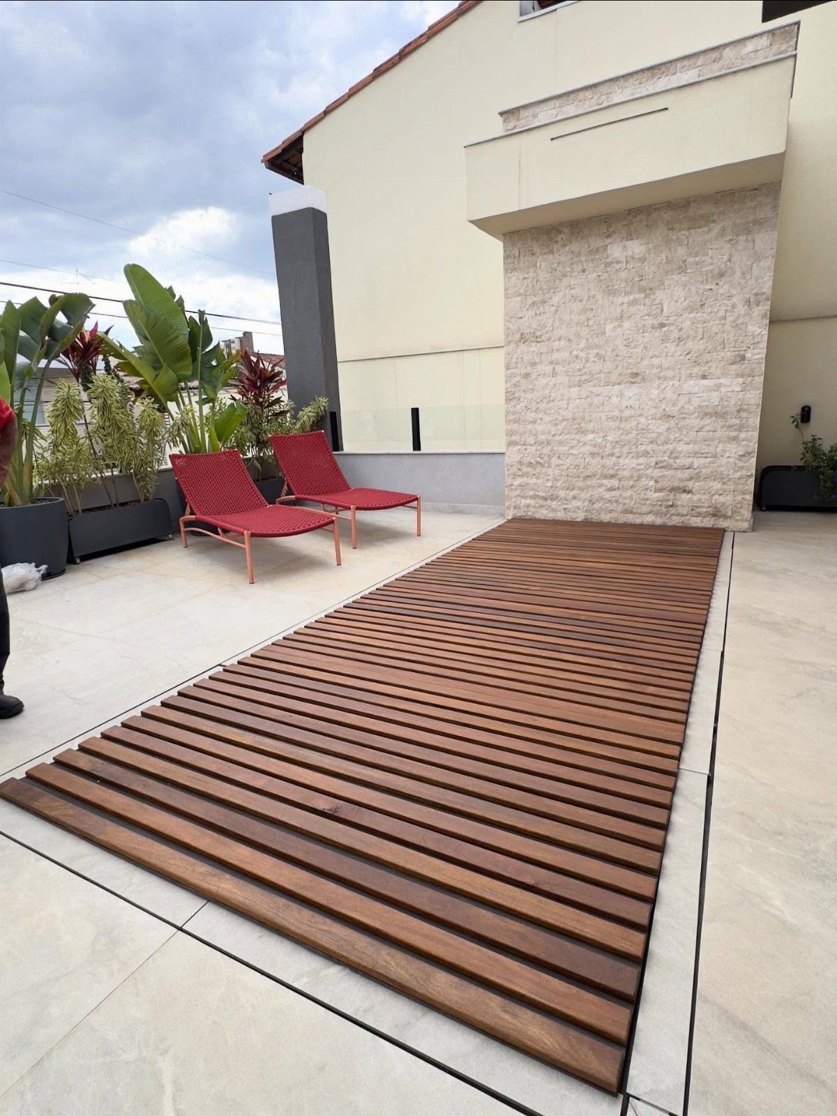Wooden deck slats laid over a light grey tiled patio with red lounge chairs.