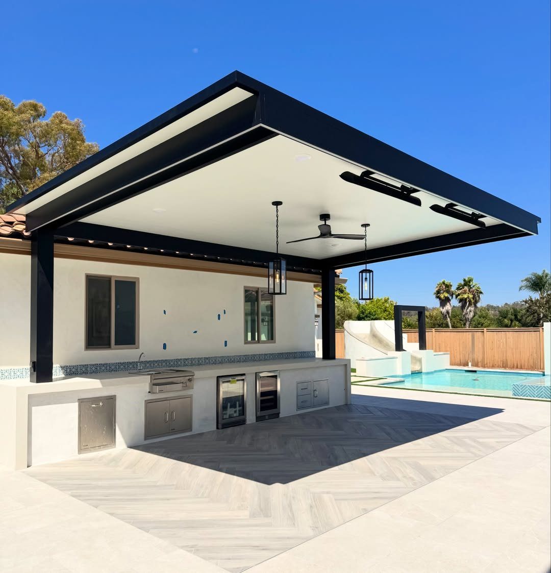 Modern outdoor kitchen with built-in grill and black patio cover next to a pool.