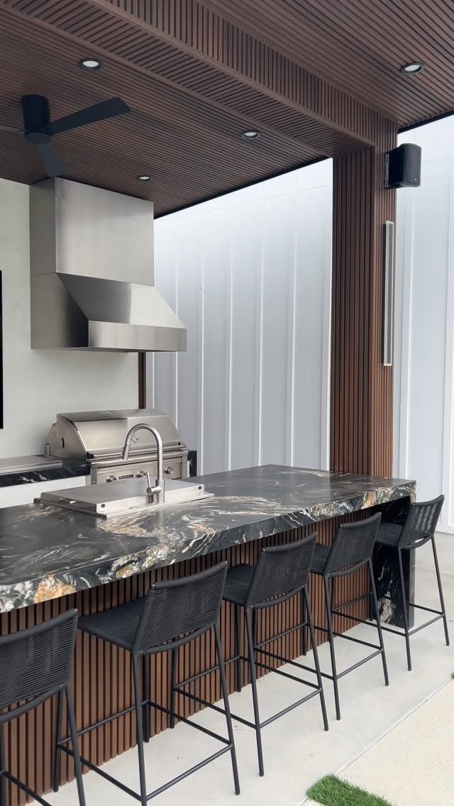 Dark marble countertop with a built-in grill and sink in a modern outdoor kitchen.