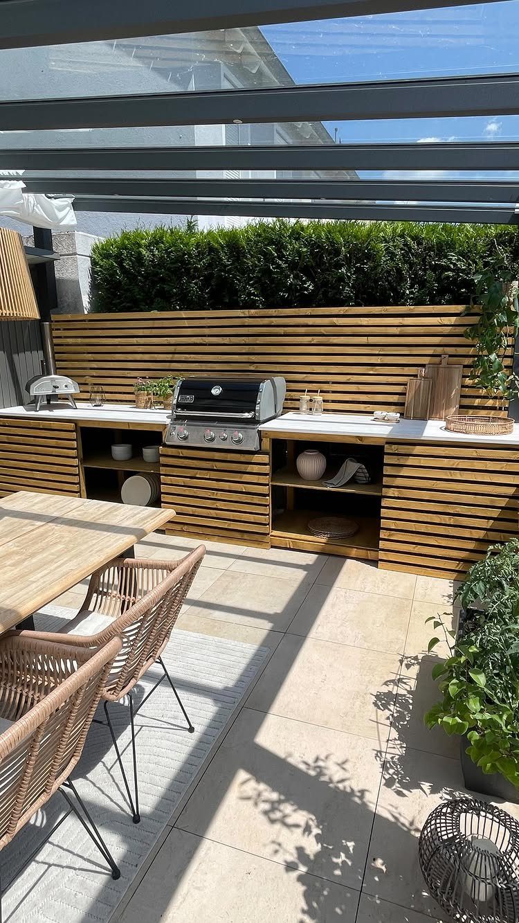 Built-in outdoor kitchen with a stainless steel grill and wooden slatted cabinetry on a patio.