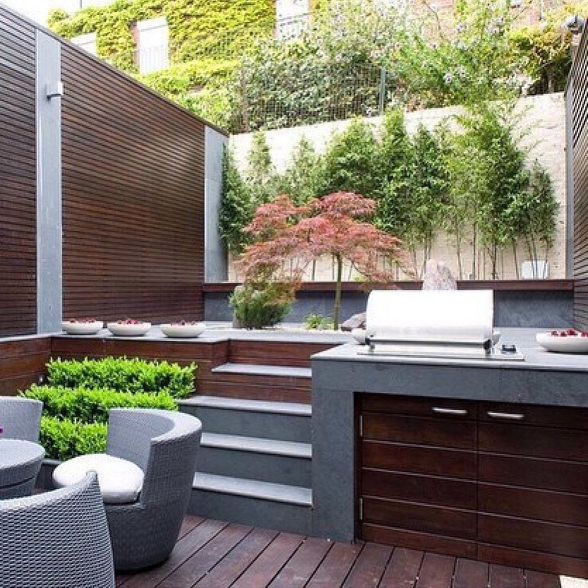 Modern outdoor kitchen with split-level dark wood decking and grey stone countertops.