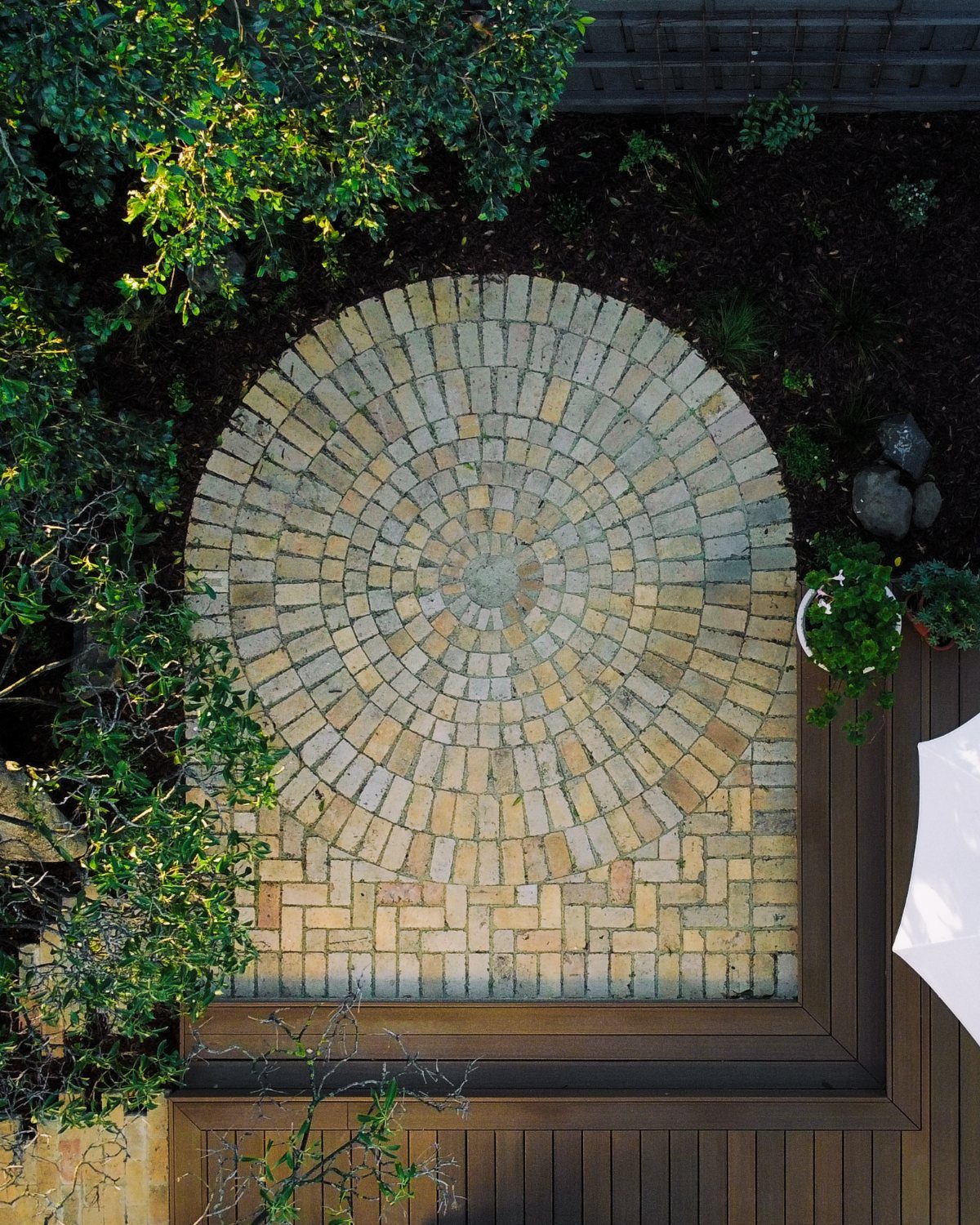 Circular brick patio design with concentric rings of tan and grey bricks in a garden.
