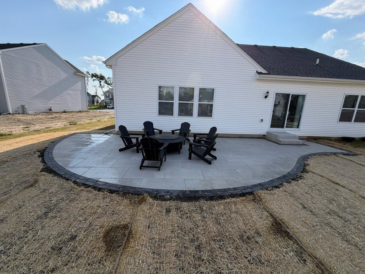 Large grey stone pavers form a curved patio with black furniture behind a white house.