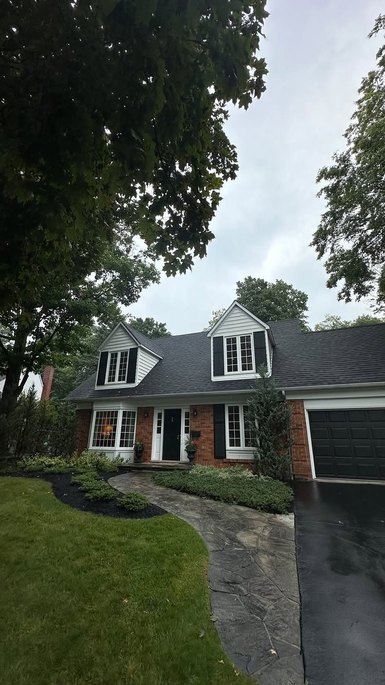 A Cape Cod house featuring two white dormer windows with black shutters under a dark roof.