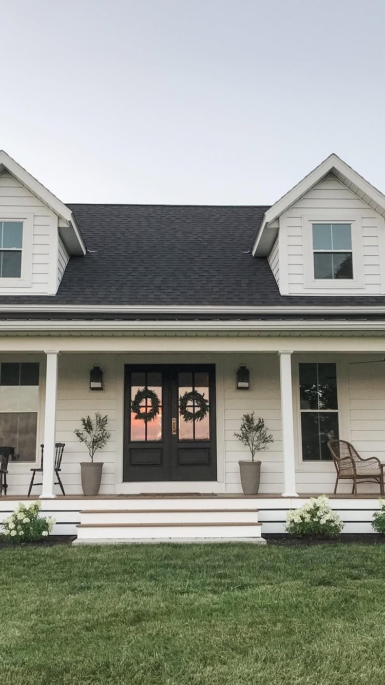 White house exterior featuring a front porch with columns, dark double doors, and potted plants.