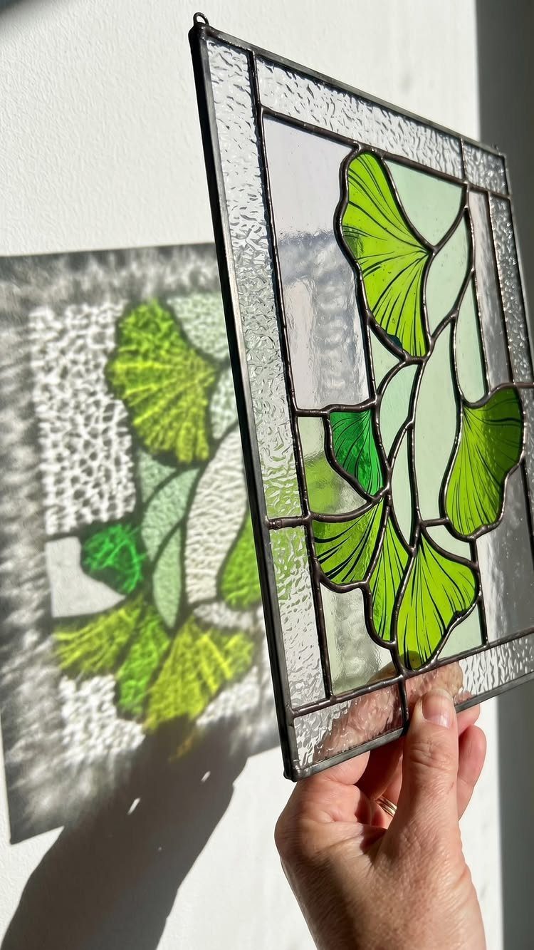 Colorful Stained Glass Design: 10 Ideas to Light a Room 8 A person holding a green ginkgo leaf stained glass panel casting a shadow on a wall.