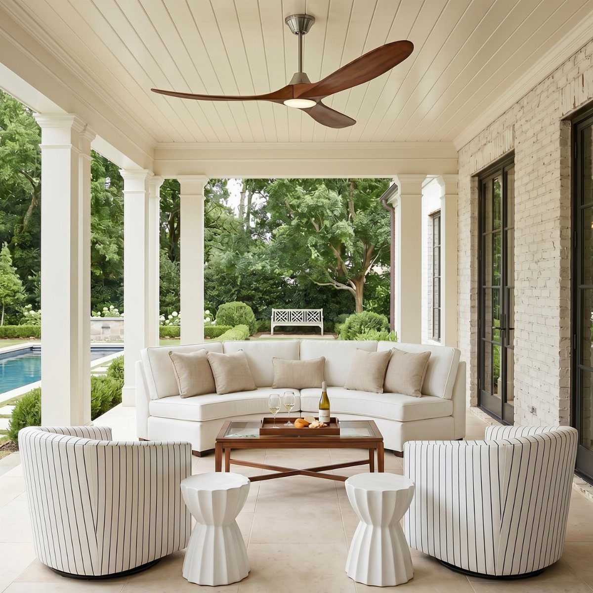 A white outdoor sectional and armchairs arranged on a covered patio under a ceiling fan.