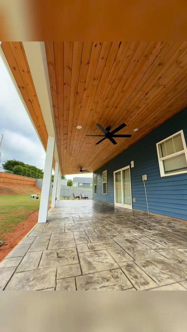 Stamped concrete patio flooring under a wooden ceiling with ceiling fans and white support pillars.