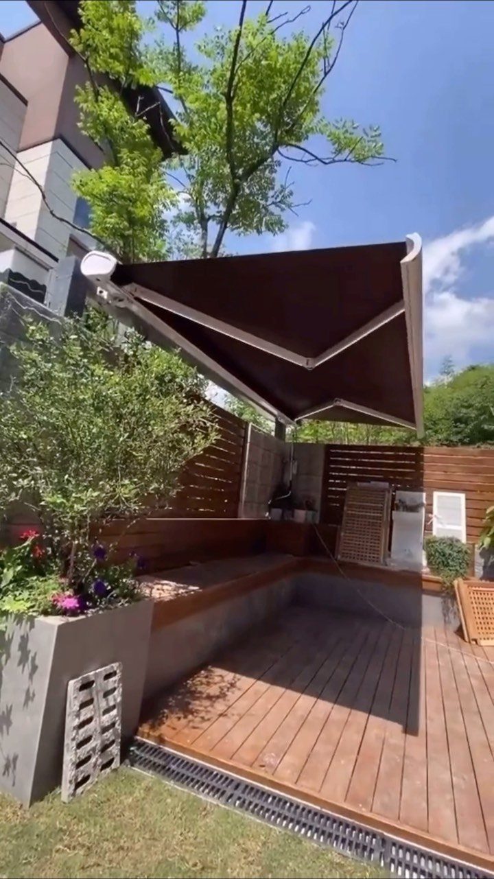 A dark brown retractable awning provides shade over a wooden deck and built-in seating area.