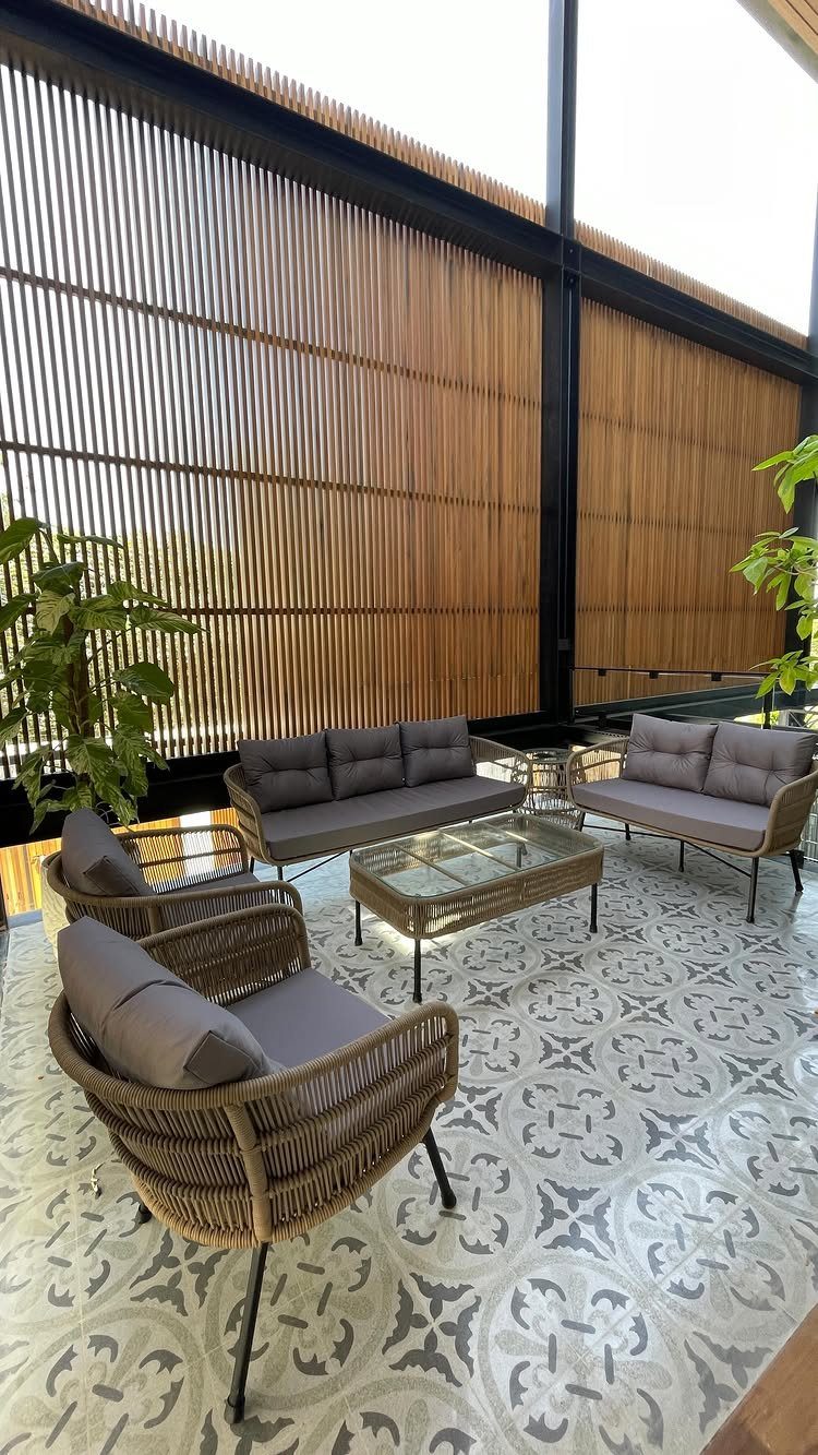 Wicker lounge chairs and sofas with grey cushions arranged around a glass coffee table on patterned tiles.