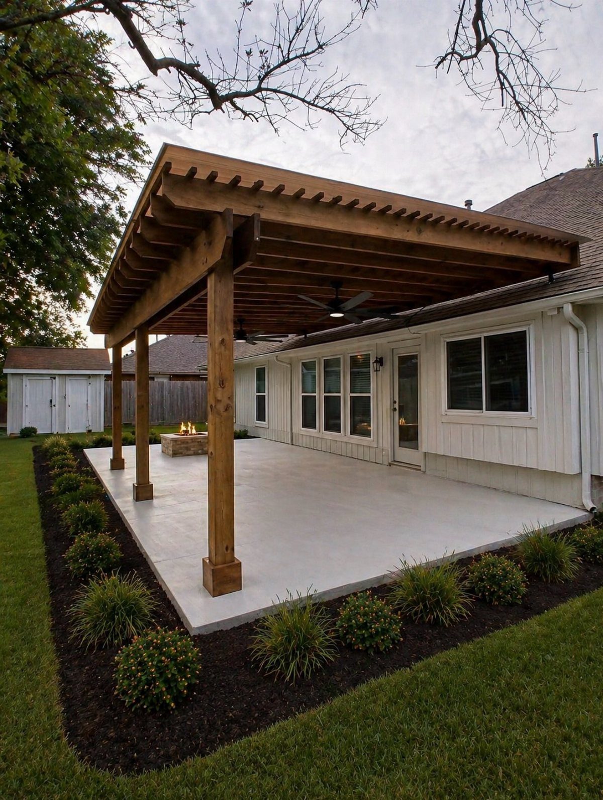 A large wooden pergola structure covering a concrete patio next to a white house.