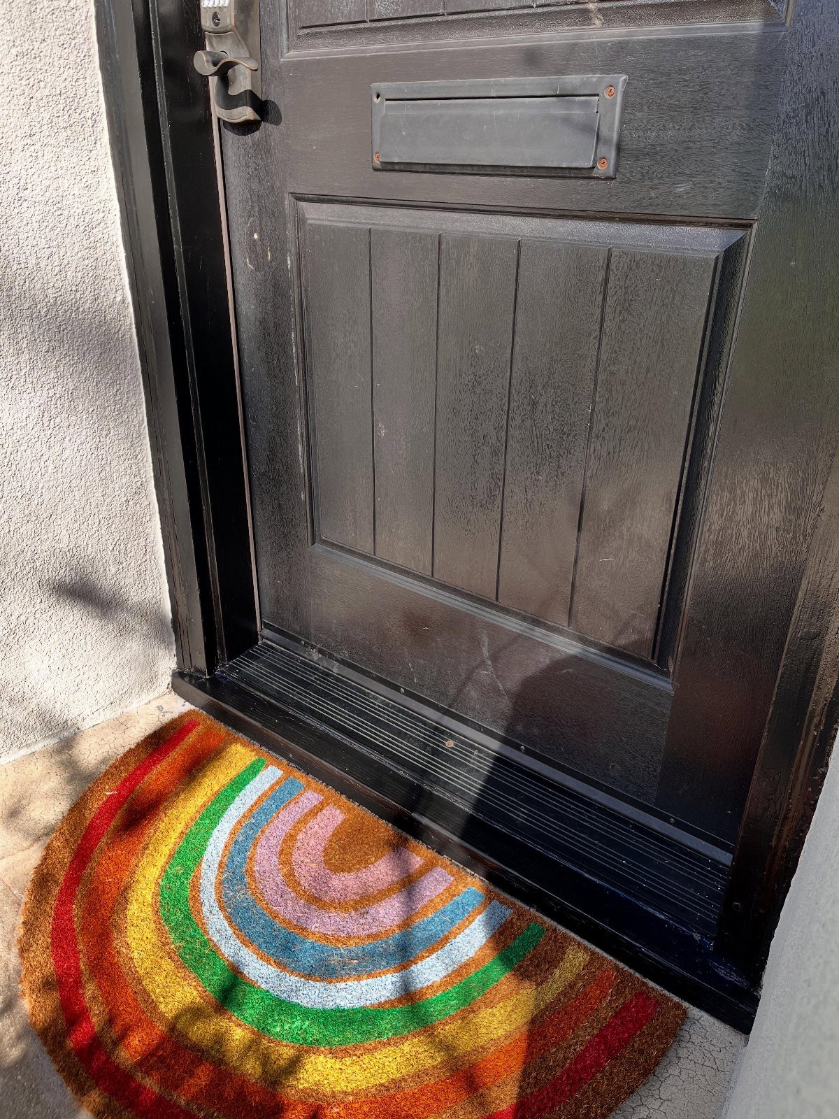 A colorful rainbow doormat placed in front of a black wooden front door.