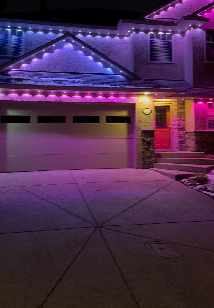 Suburban house exterior at night featuring vibrant pink and blue LED lighting along the roof and garage.