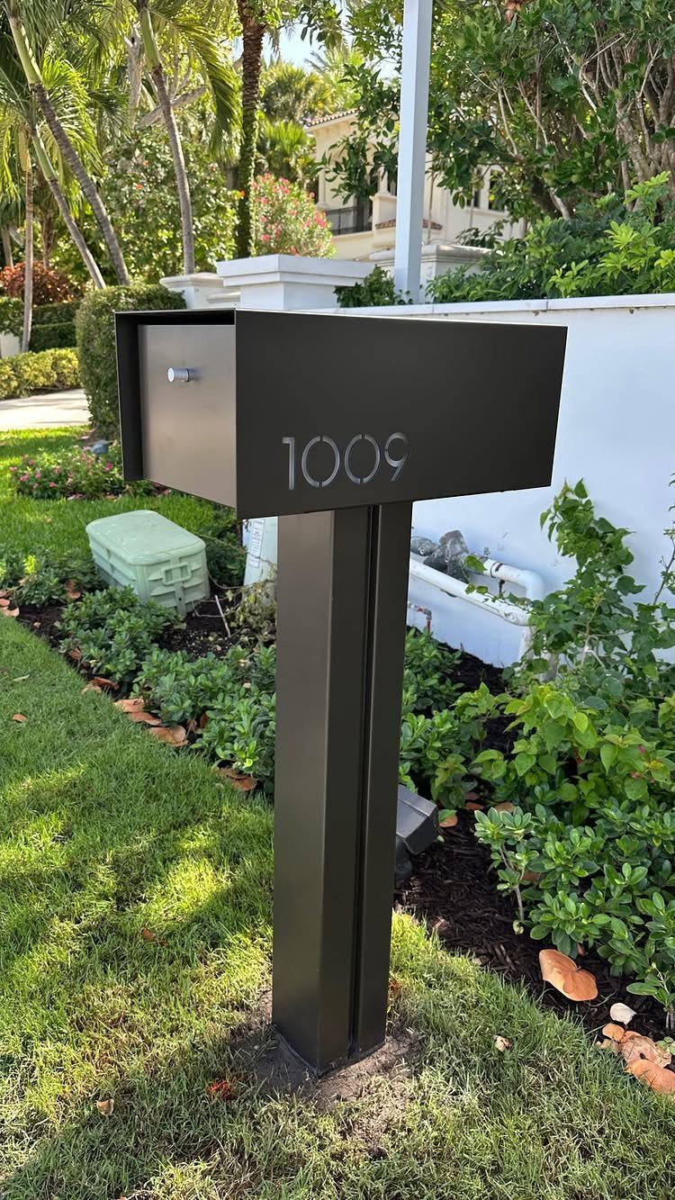Modern matte black mailbox with the number 1009 standing in a green garden lawn.