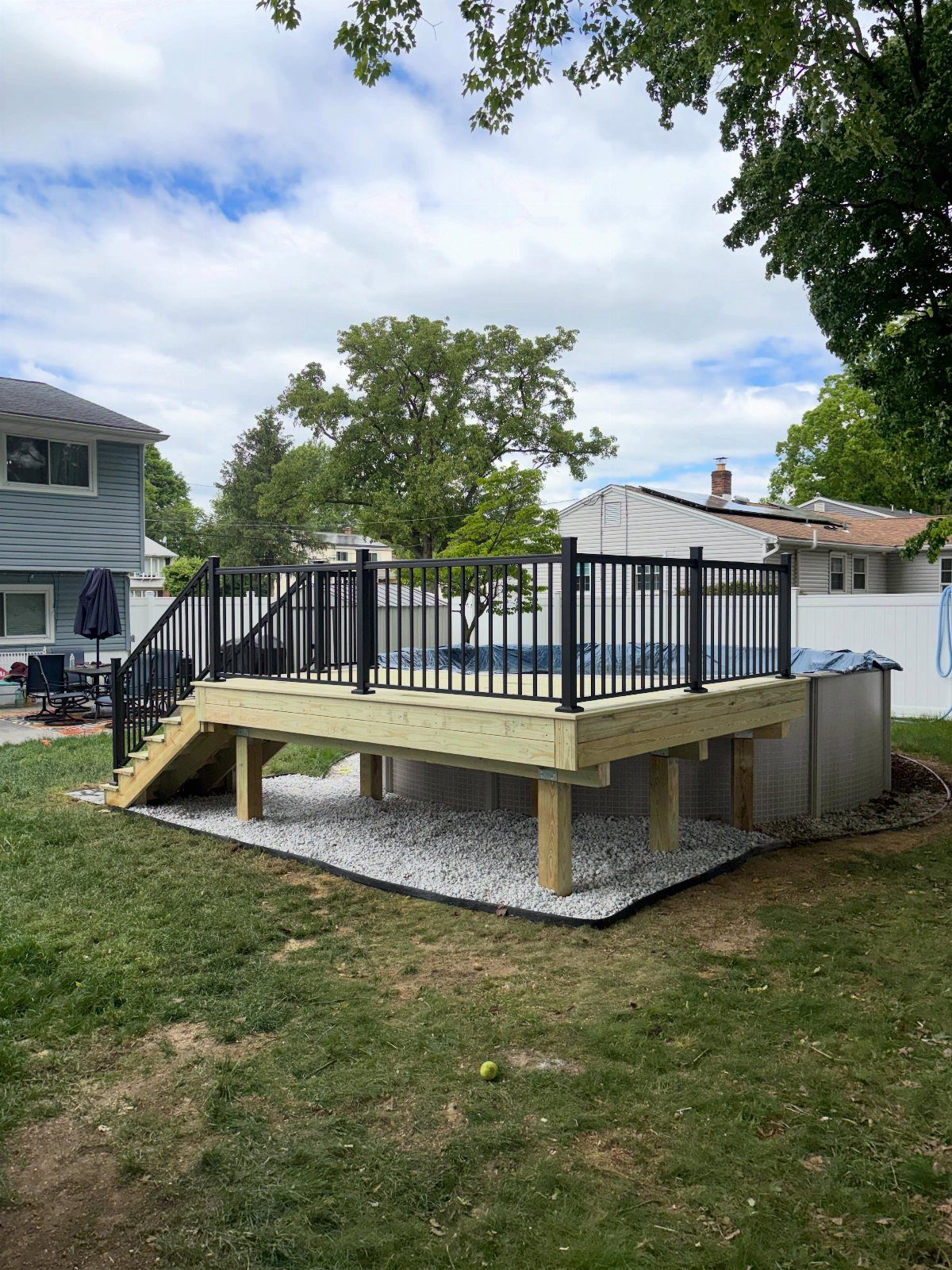 A wooden partial deck with black railings built around the side of an above-ground pool.