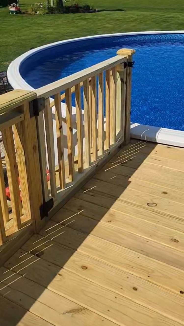 Wooden deck railing and a hinged gate surrounding a blue above-ground swimming pool.