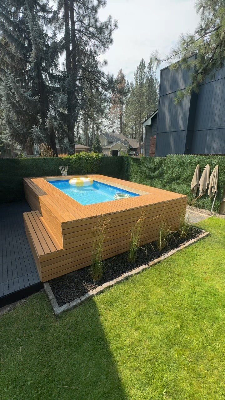 A light brown wooden deck built around a small rectangular above-ground pool in a grassy yard.