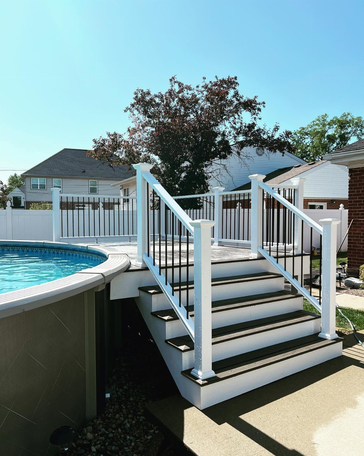 A white wooden deck with black railings built around a circular above-ground swimming pool.