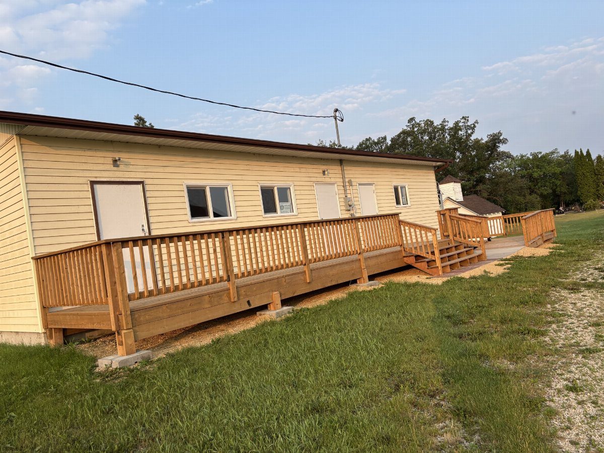 A long wooden accessibility ramp with railings attached to a yellow building next to a grass field.