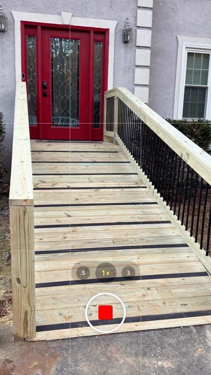A wooden accessibility ramp with black non-slip strips leading to a red front door.