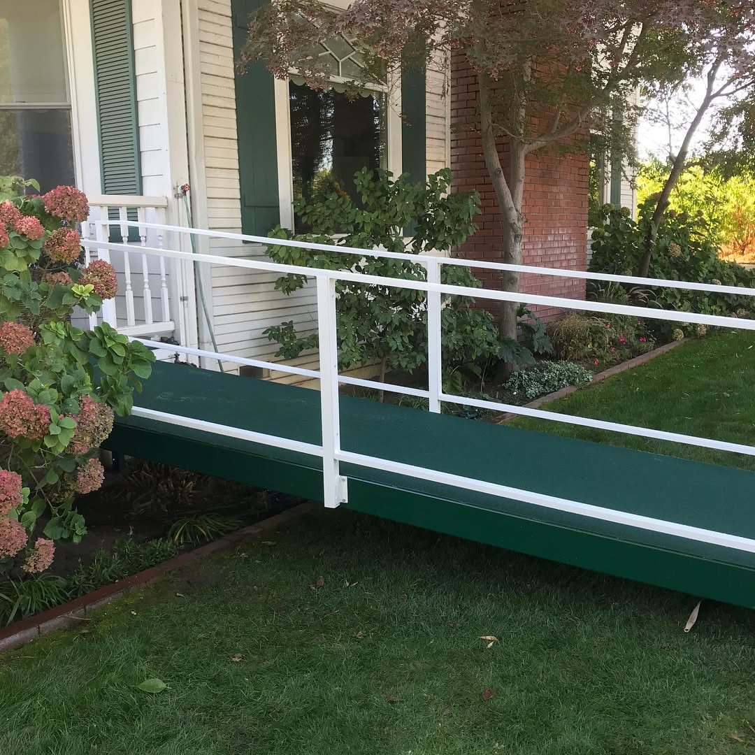 A dark green wooden accessibility ramp with white railings installed on a grassy lawn by a house.