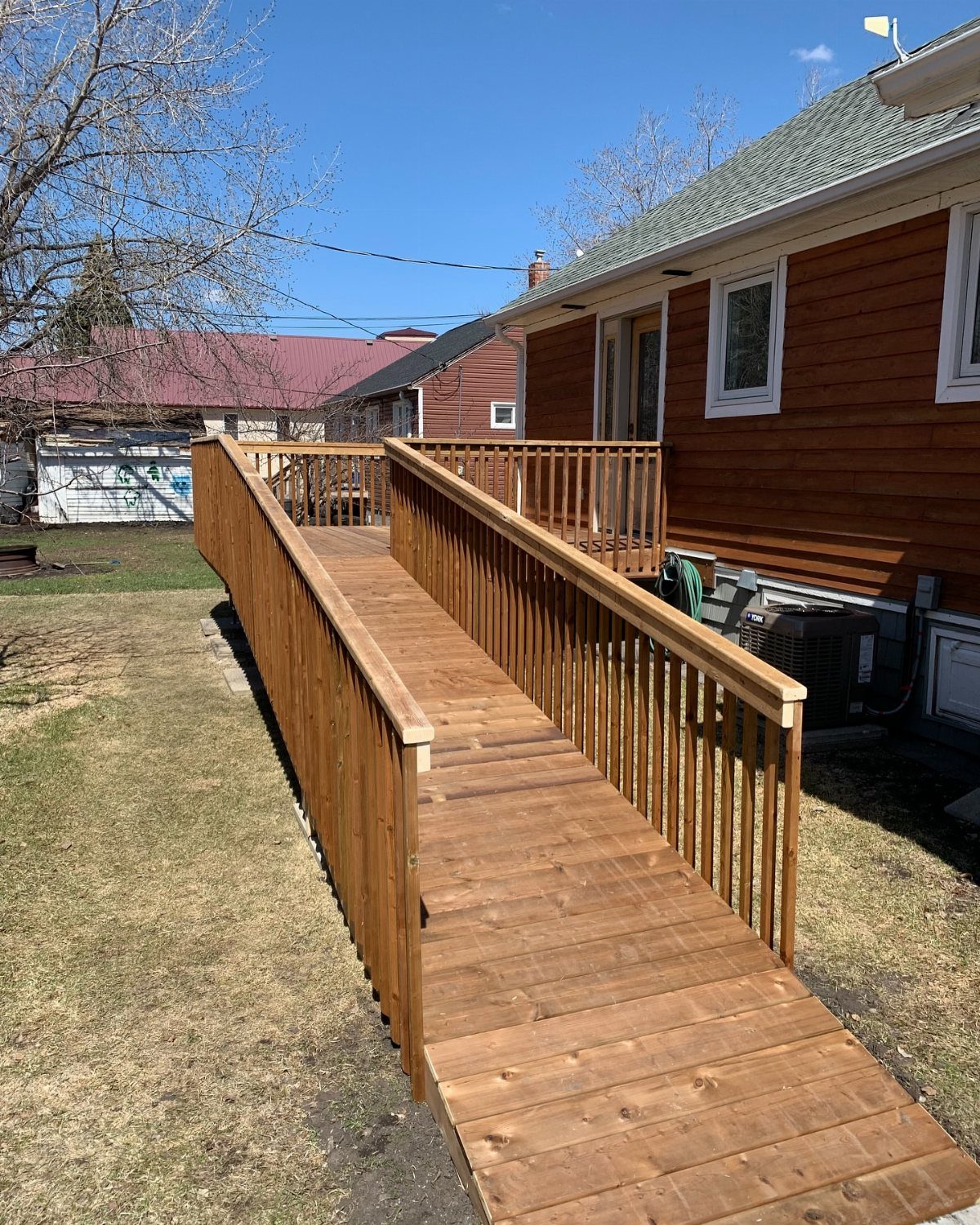 A long wooden accessibility ramp with railings leading up to a house deck.
