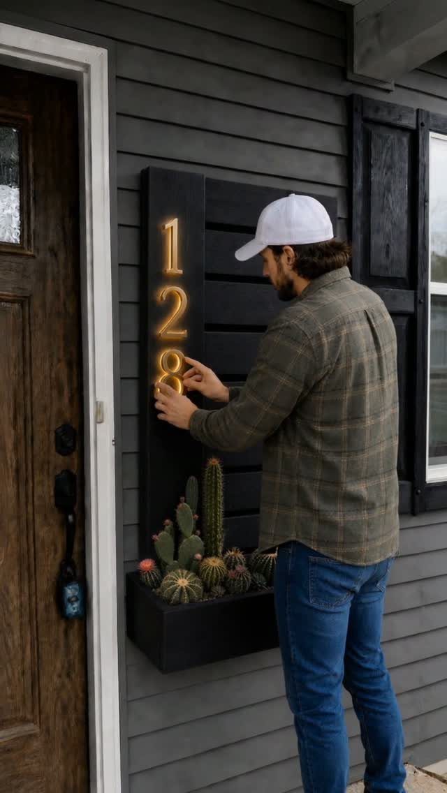 A man adjusting glowing house numbers on a black vertical wall planter containing small cacti.