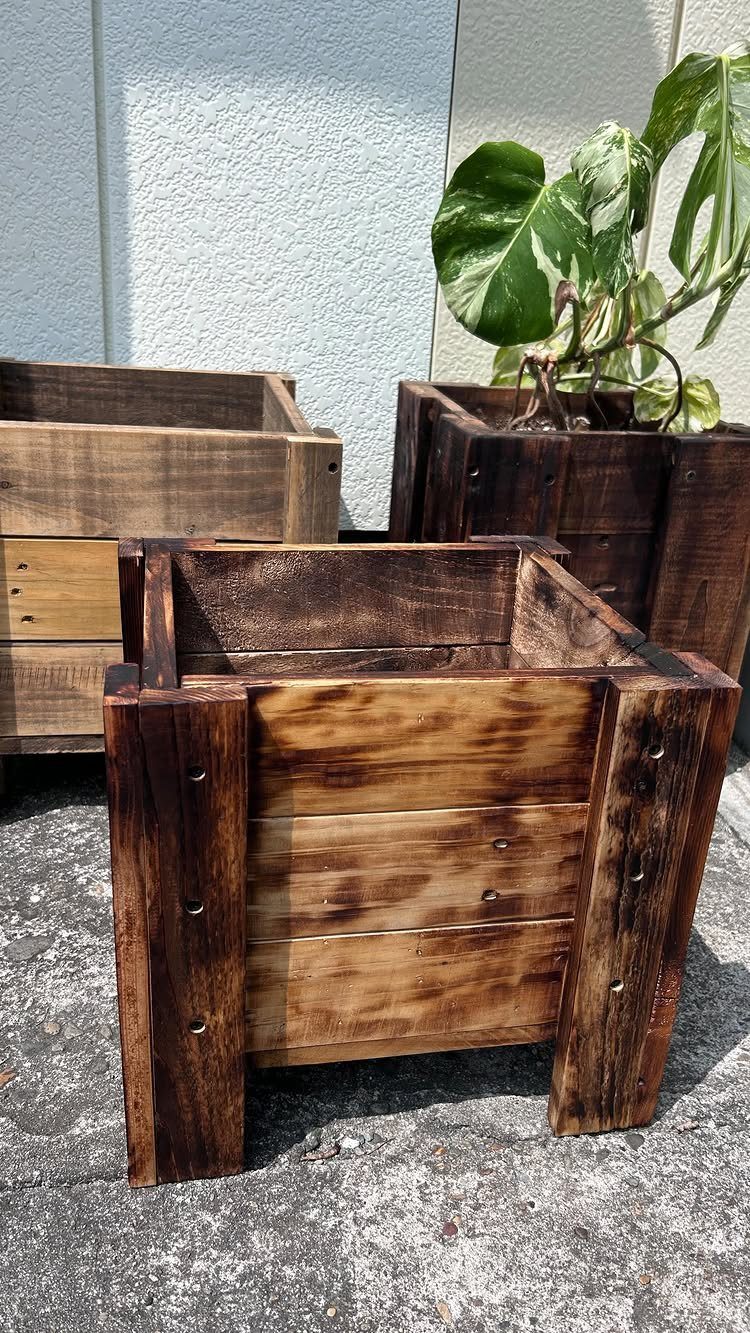 Three dark stained wooden planter boxes sitting on a concrete ground outdoors.