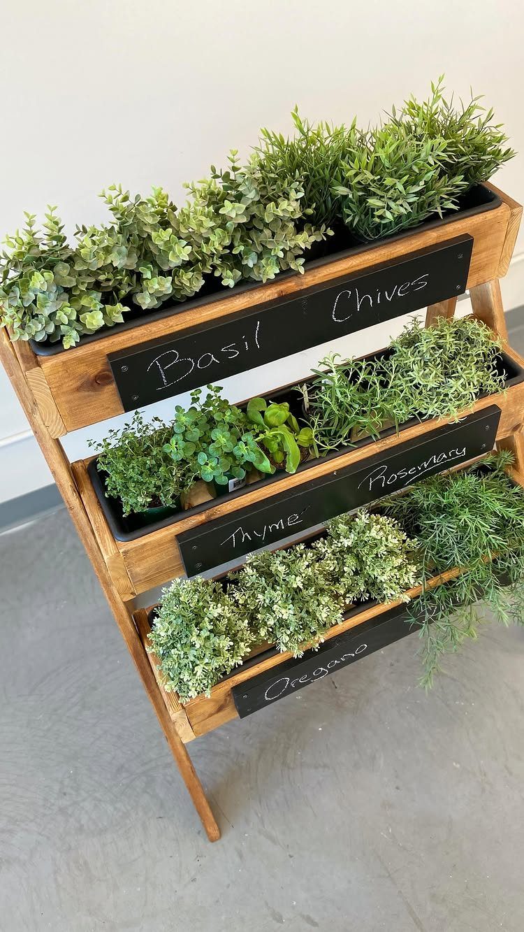 A wooden three-tiered herb planter containing various green plants with chalkboard labels for each herb.