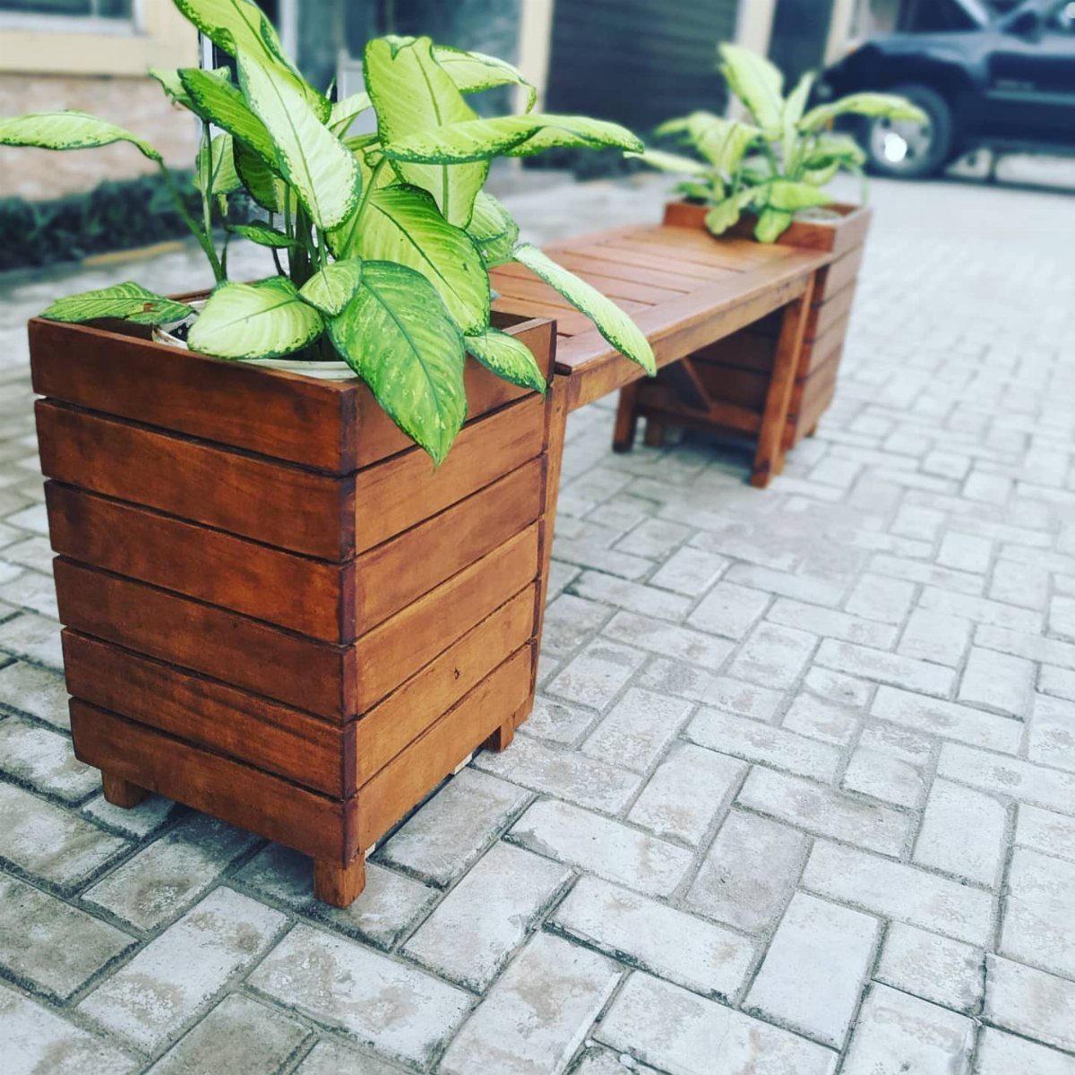 A long wooden planter bench with green plants in integrated boxes on a brick patio.