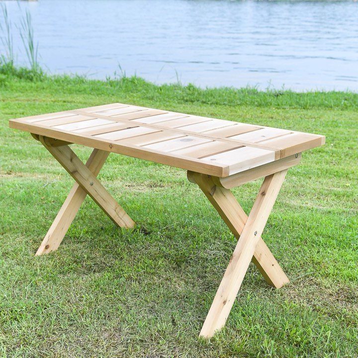 Easy Patio Table DIY: 8 Projects for Your Yard 7 A light wood rectangular table with X-shaped legs stands on green grass by a lake.